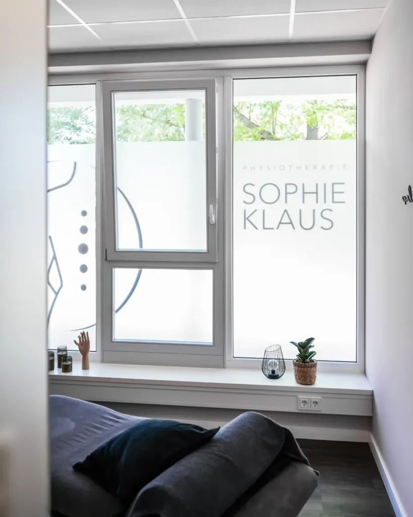 Behandlungsraum der Physiotherapie Sophie Klaus mit Milchglasfenster, Logo-Schriftzug und gemütlicher Liege.
